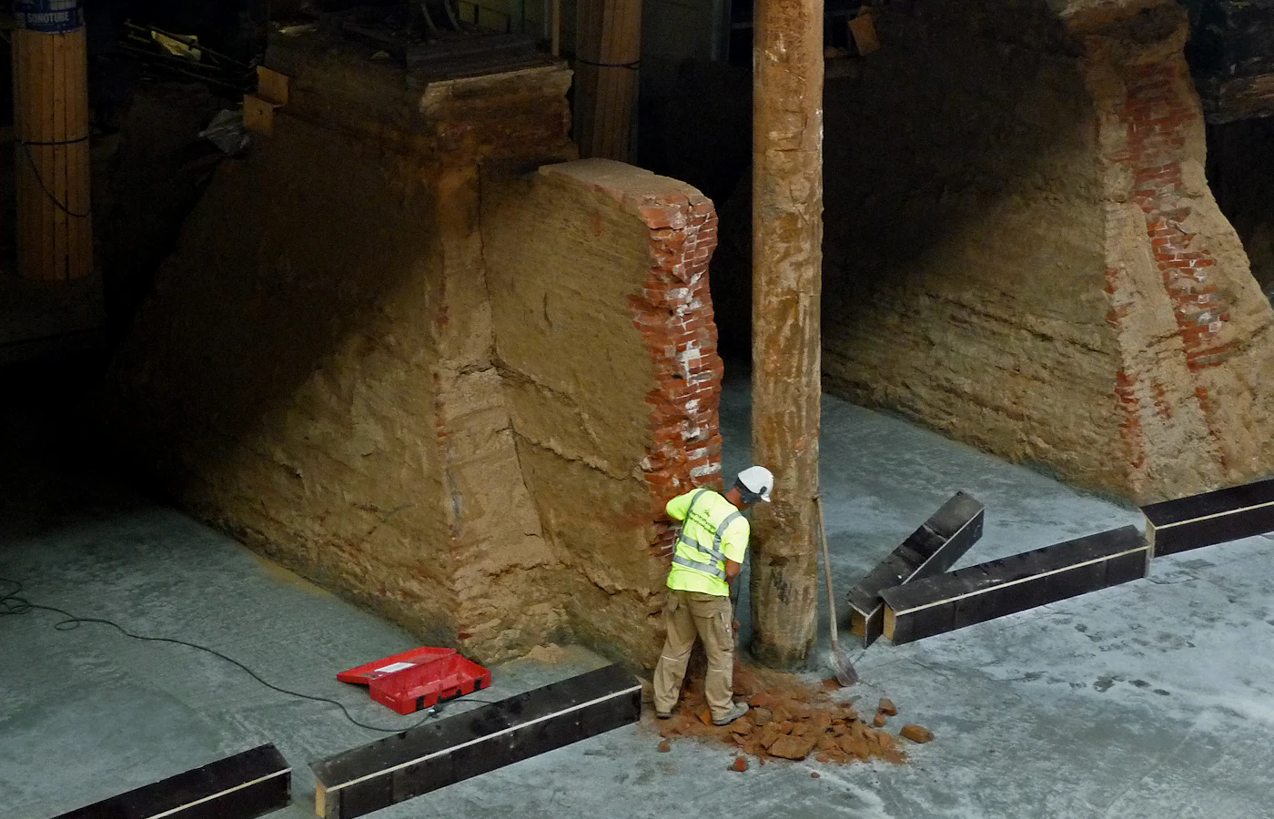 Worker excavating beneath an existing foundation during underpinning (stock photo)