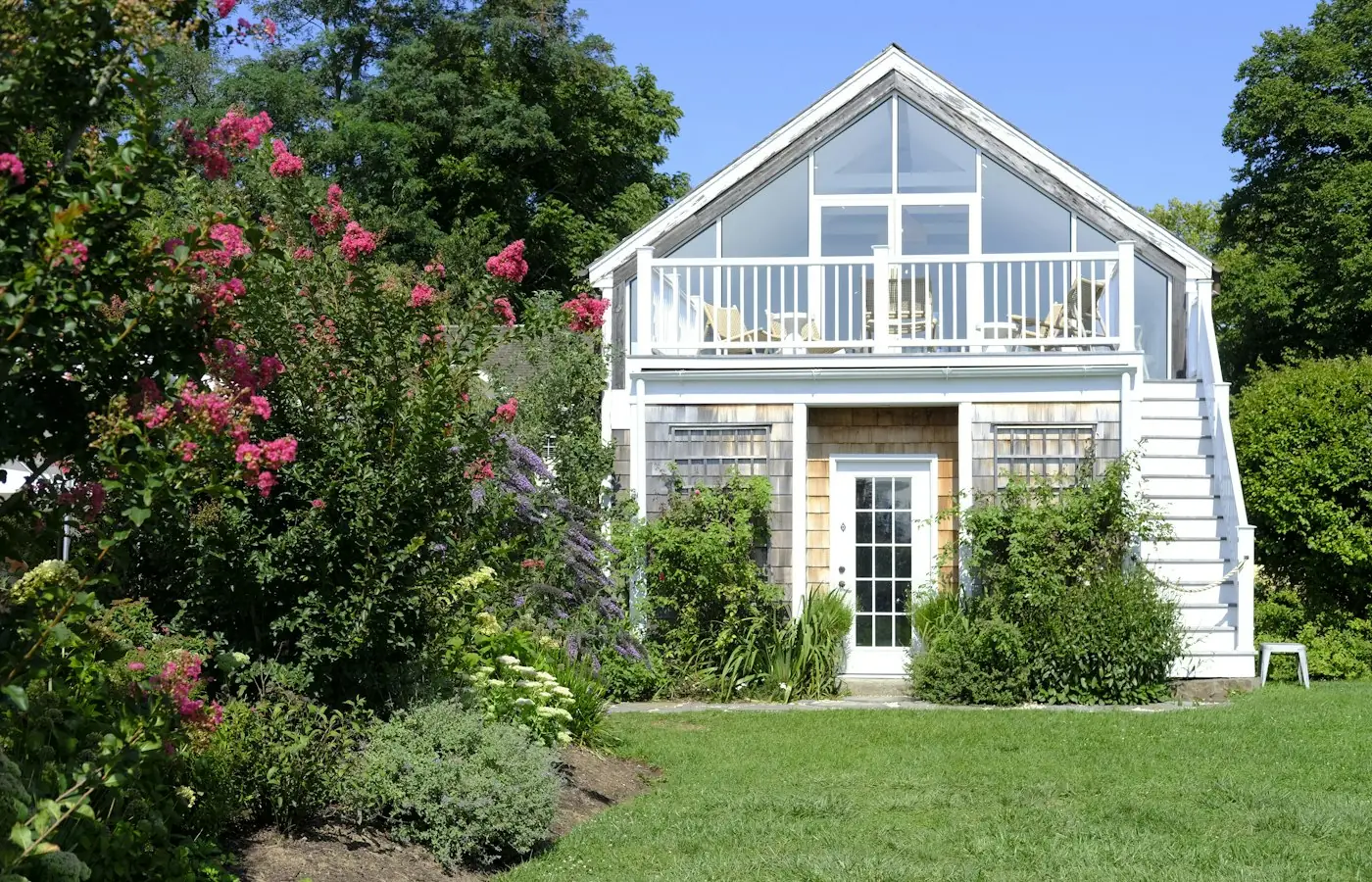 Finished two-story backyard cottage with balcony and large windows, a detached ADU example (stock photo)