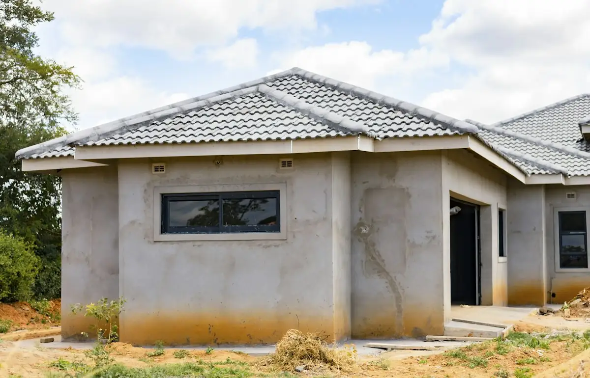A house with grey concrete walls and a tiled roof under a blue sky (stock photo)