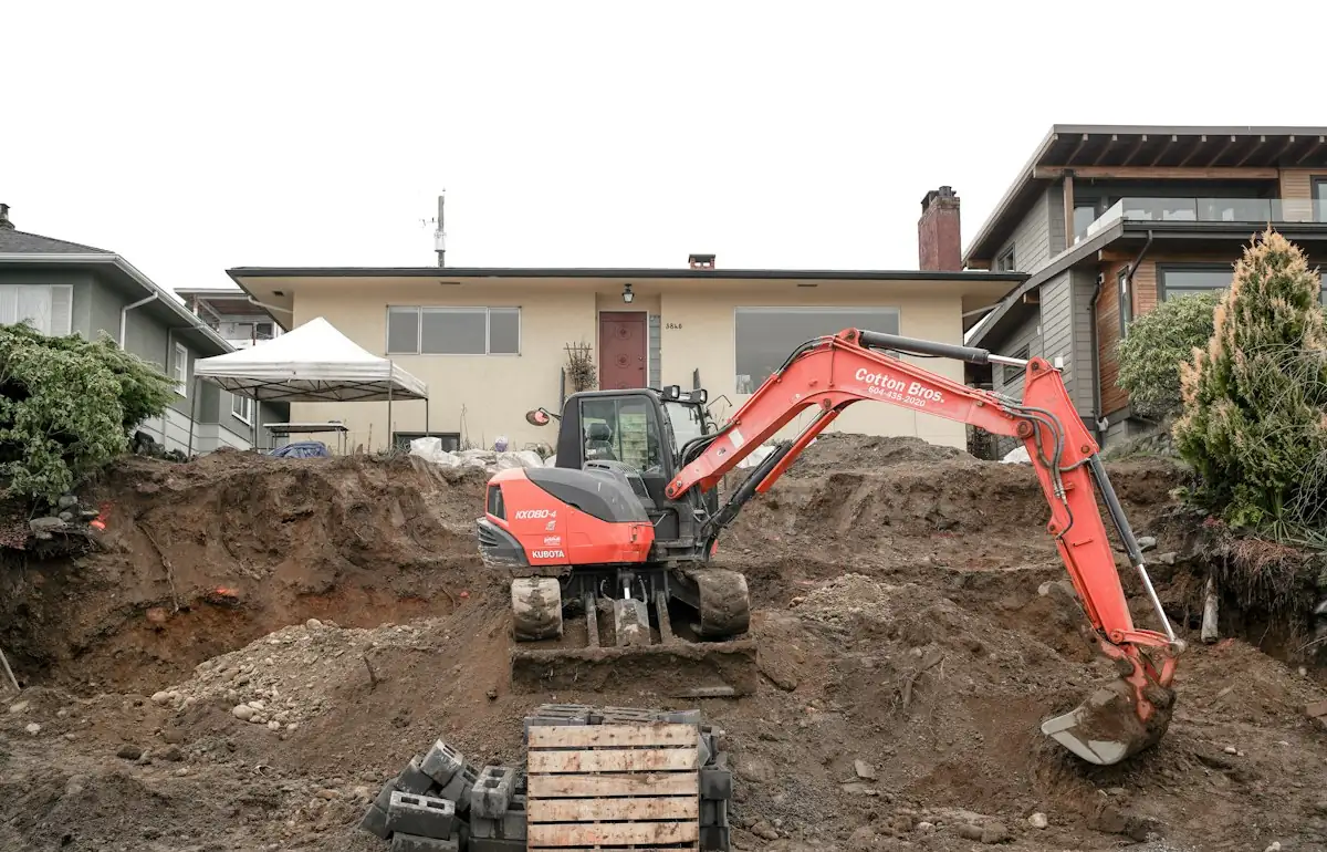 A red excavator digging a pile of dirt in front of a house (stock photo)